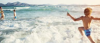 Kinder spielen im Meer mit Berge im Hintergrund.