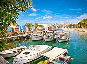 Petits bateaux amarrés dans le port de Saranda, avec palmiers et maisons au bord de l’eau