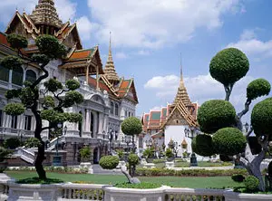 Vue du Grand Palais de Bangkok avec ses toits dorés et ses jardins soignés sous un ciel bleu.