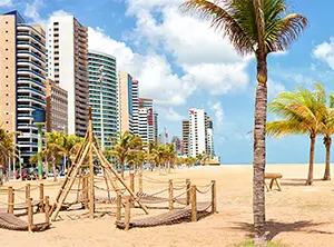 Blick auf die Strandpromenade in Fortaleza, Brasilien, umgeben von modernen Hochhäusern und Sandstrand mit Palmen.
