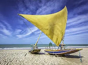 Fischerboote mit farbigen Segeln am Sandstrand von Natal, Brasilien, unter einem blauen Himmel.