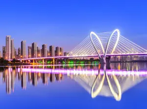 Skyline von Shenyang bei Abenddämmerung, reflektiert im Wasser, mit beleuchteter Brücke.