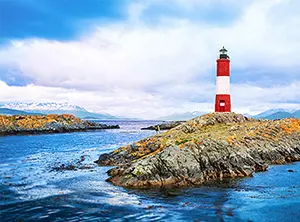 Leuchtturm auf einer Insel in Feuerland, umgeben von Gewässern und Bergen im Hintergrund.