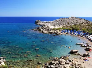 Petite crique aux eaux turquoise à Rhodes, entourée de rochers et équipée de transats en bord de mer.