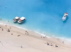 Plage de sable avec eau turquoise et bateaux près du rivage à Zakynthos
