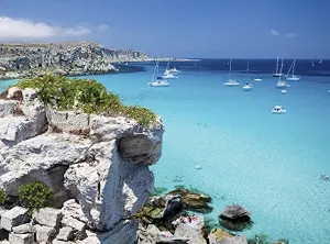 Côte rocheuse en Sicile avec mer turquoise et voiliers au large