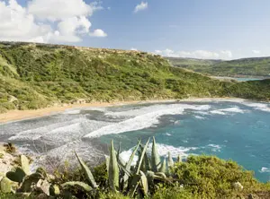 Crique avec eau turquoise entourée de falaises et végétation à Malte