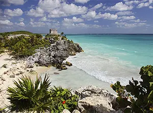 Plage de sable blanc avec eau turquoise et ruines mayas sur une falaise à Tulum