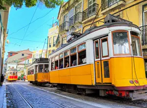 Le célèbre tramway 28 traversant une rue étroite de Lisbonne, bordée de bâtiments colorés et de balcons typiques.