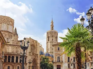 Place historique à Valence avec une cathédrale gothique, un clocher élancé, des palmiers et des lampadaires traditionnels.