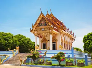 Temple bouddhiste aux toits décorés entouré de végétation tropicale en Thaïlande