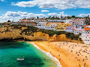 Plage de sable doré bordée de falaises et de maisons blanches sur la côte de l’Algarve, au Portugal.