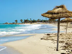 Plage de sable doré à Djerba avec des parasols en paille et la mer turquoise sous un ciel ensoleillé.