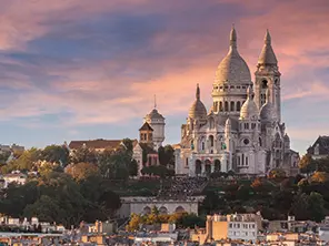 Vue sur la basilique du Sacré-Cœur à Montmartre au coucher du soleil, dominant les toits de Paris.