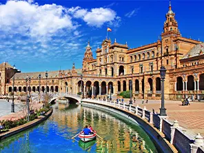 Die Plaza de España in Sevilla mit ihrem Kanal und einem Ruderboot, unter einem strahlend blauen Himmel.