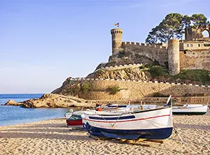 Strand an der Costa Brava mit historischem Burgturm und Fischerboot