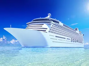 Weißes Kreuzfahrtschiff unter blauem Himmel, von der Seite angestrahlt.
