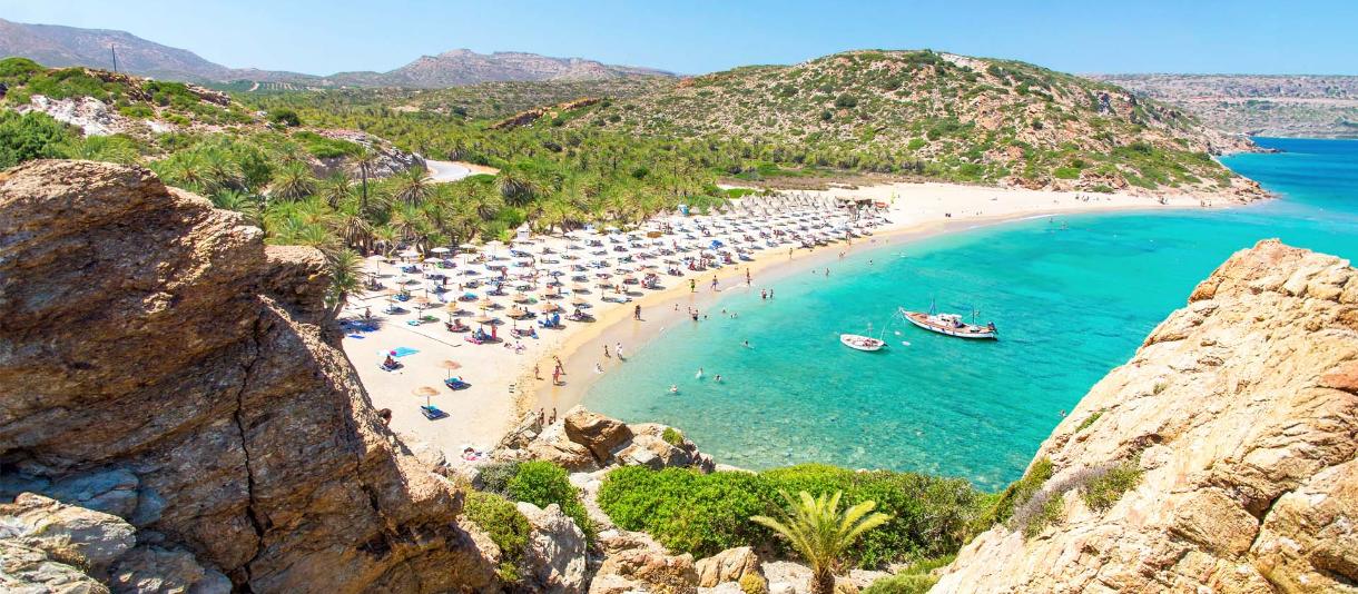 Kreta: Blick auf Palmenstrand von Vai mit türkisblauem Meer und Badegästen unter Strohsonnenschirmen