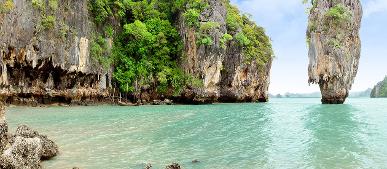 Eine steile Kalksteinnadel ragt im smaragdgrünen Wasser vor einer bewachsenen Felswand auf der James-Bond-Insel in Thailand empor.